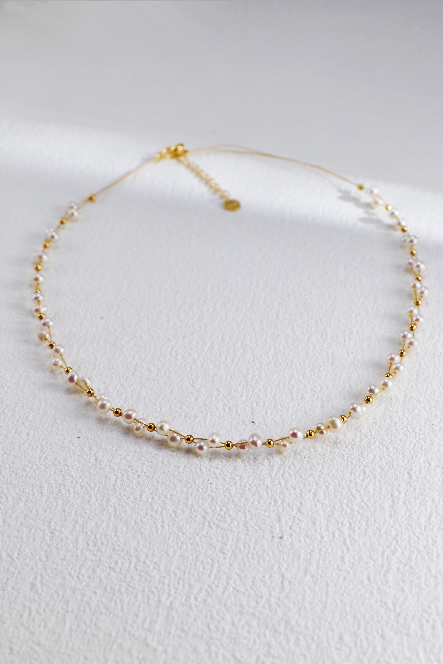 A delicate 18K Gold Plated 925 Silver Handcrafted Freshwater Pearl Necklace by Siren Mode with gold beads arranged alternately along a thin chain lays on a light, textured surface. The necklace clasps at the back with a short extension chain and a small round pendant.