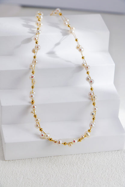 Siren Mode's 18K Gold Plated 925 Silver Handcrafted Freshwater Pearl Necklace showcases small white pearls and glossy gold plated beads, gracefully arranged on a stepped white platform. The pearls and beads are evenly spaced along a delicate string, creating a refined and elegant look.