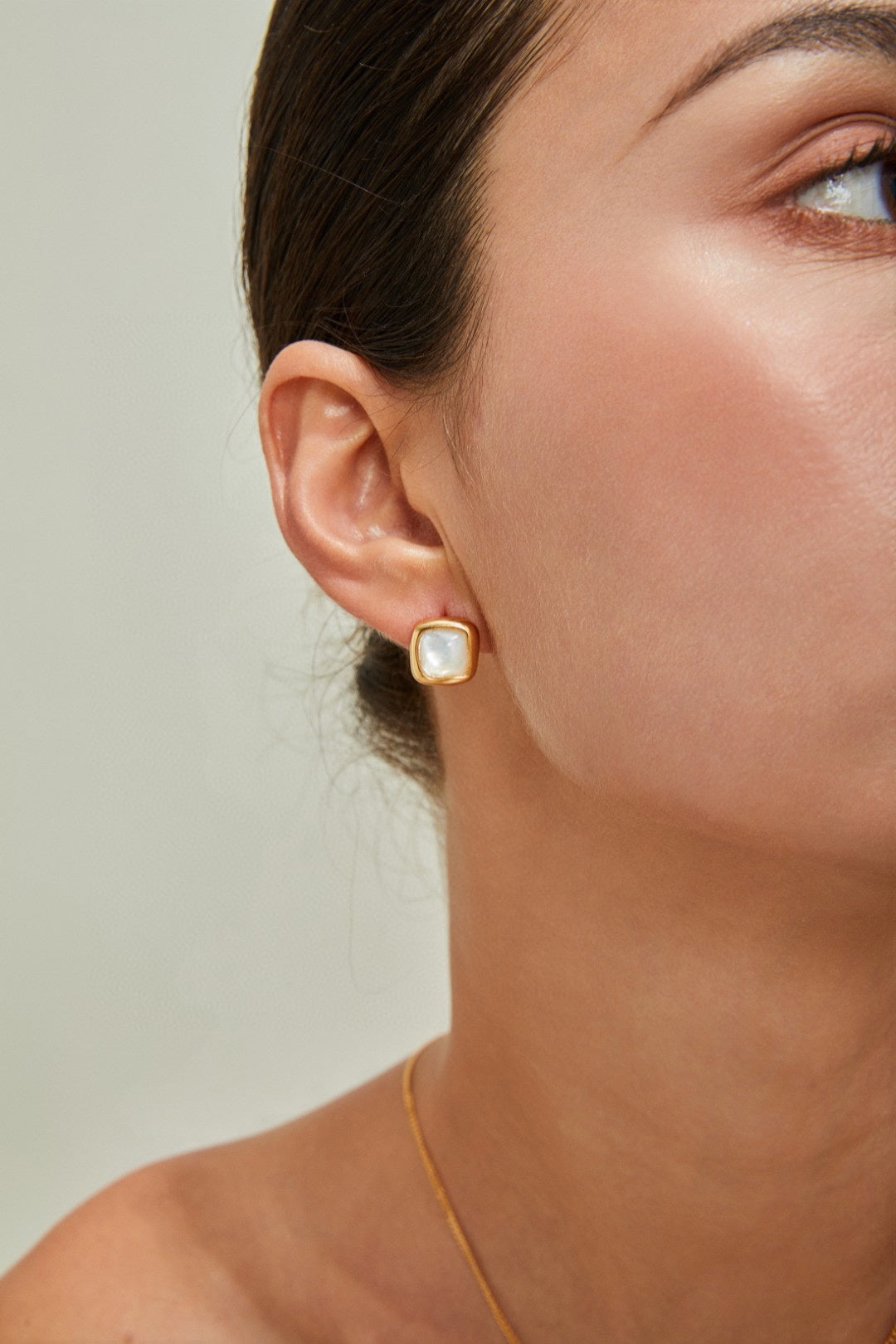 Close-up of a person wearing a Siren Mode 18K Gold Plated 925 Silver Square Baroque Pearl Stud Earring. The person has their hair pulled back, revealing a smooth complexion and minimal makeup. The neutral background highlights the earring as the main subject.