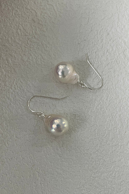 A pair of Siren Mode 925 Silver Foil Baroque Pearl Drop Earrings featuring teardrop-shaped baroque pearls with silver hooks, displayed on a textured white surface. The pearls exhibit a soft pinkish-white sheen.