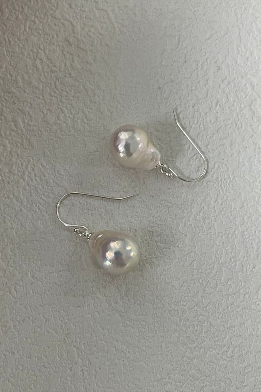 A pair of Siren Mode 925 Silver Foil Baroque Pearl Drop Earrings featuring teardrop-shaped baroque pearls with silver hooks, displayed on a textured white surface. The pearls exhibit a soft pinkish-white sheen.