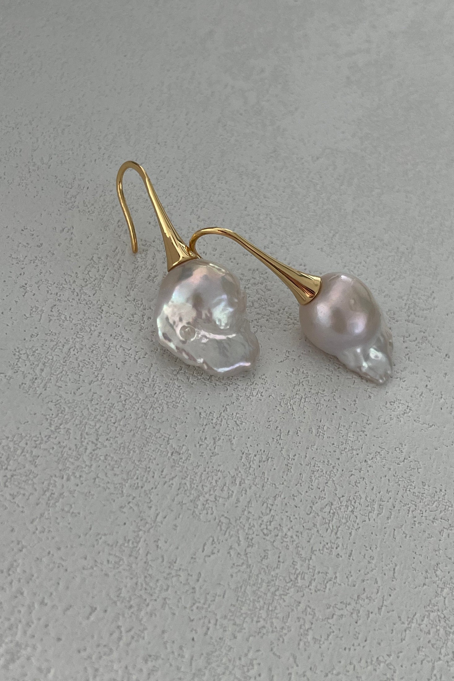 The "Baroque Pearl Drop Earrings - 18k Gold Plated Silver" by Siren Mode feature irregularly shaped, glossy white baroque pearls set in gold-plated silver hooks, elegantly displayed against a lightly textured background.