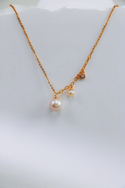 Siren Mode's Elegant Freshwater Pearl Necklace in Sterling Silver features a minimalist design with two dangling freshwater pearls of different sizes and a small, glittering diamond accent. The smooth, white surface backdrop highlights the elegance and simplicity of this exquisite jewelry piece.