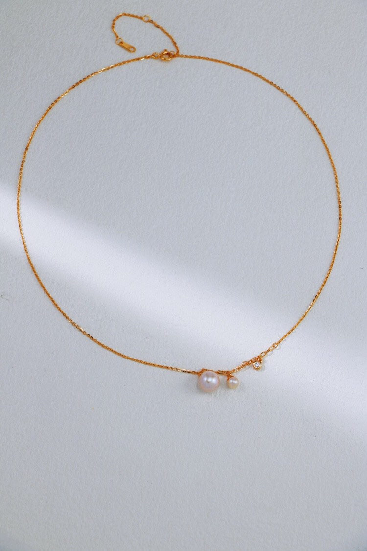 An Elegant Freshwater Pearl Necklace made of sterling silver by Siren Mode is pictured against a light background. The delicate necklace features two small freshwater pearls of different sizes, positioned close together near the center of the chain.