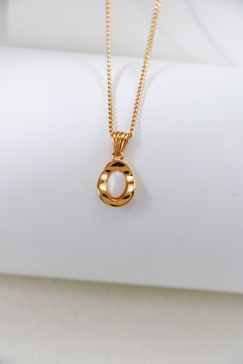 The Elegant Gold-Plated Sterling Silver Necklace with Teardrop Pendant by Siren Mode features an oval white stone at its center. This delicate necklace, displayed on a white, rolled fabric background, offers an adjustable length for the perfect fit.