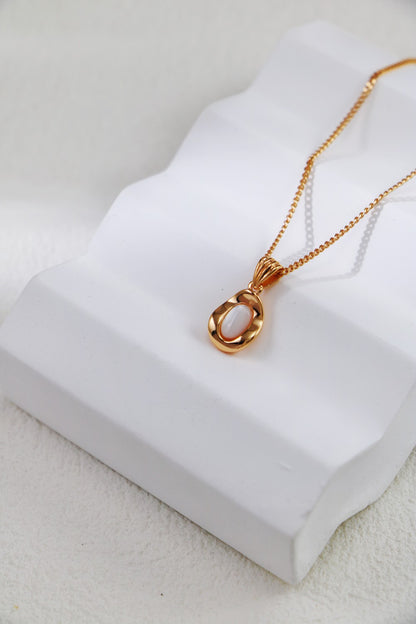 An Elegant Gold-Plated Sterling Silver Necklace with a teardrop pendant from Siren Mode is gracefully showcased on a white sculpted stand. The softly textured background accentuates the design's delicate and refined appearance.