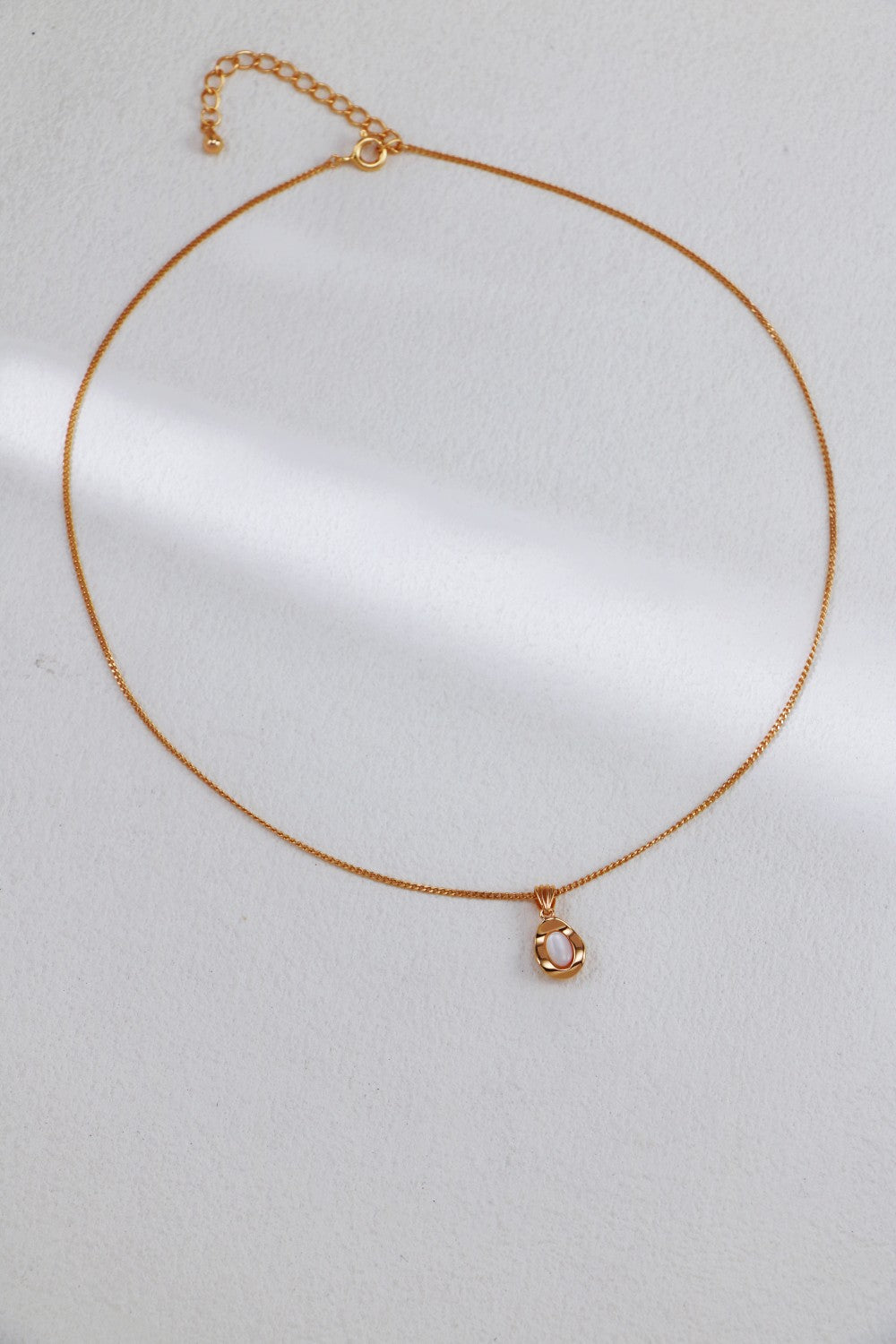 A sophisticated Elegant Gold-Plated Sterling Silver Necklace with a thin chain and adjustable length by Siren Mode, featuring a small teardrop-shaped pendant adorned with a pearl-like center. This exquisite piece is showcased on a light, neutral background.