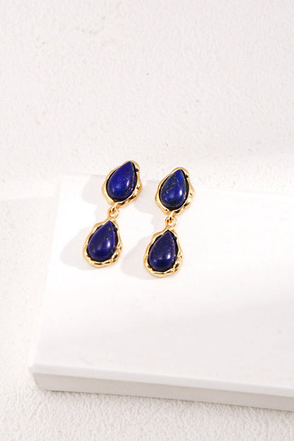 The Elegant Lapis Lazuli Teardrop Earrings in Vintage Gold by Siren Mode rest gracefully on a textured white surface.