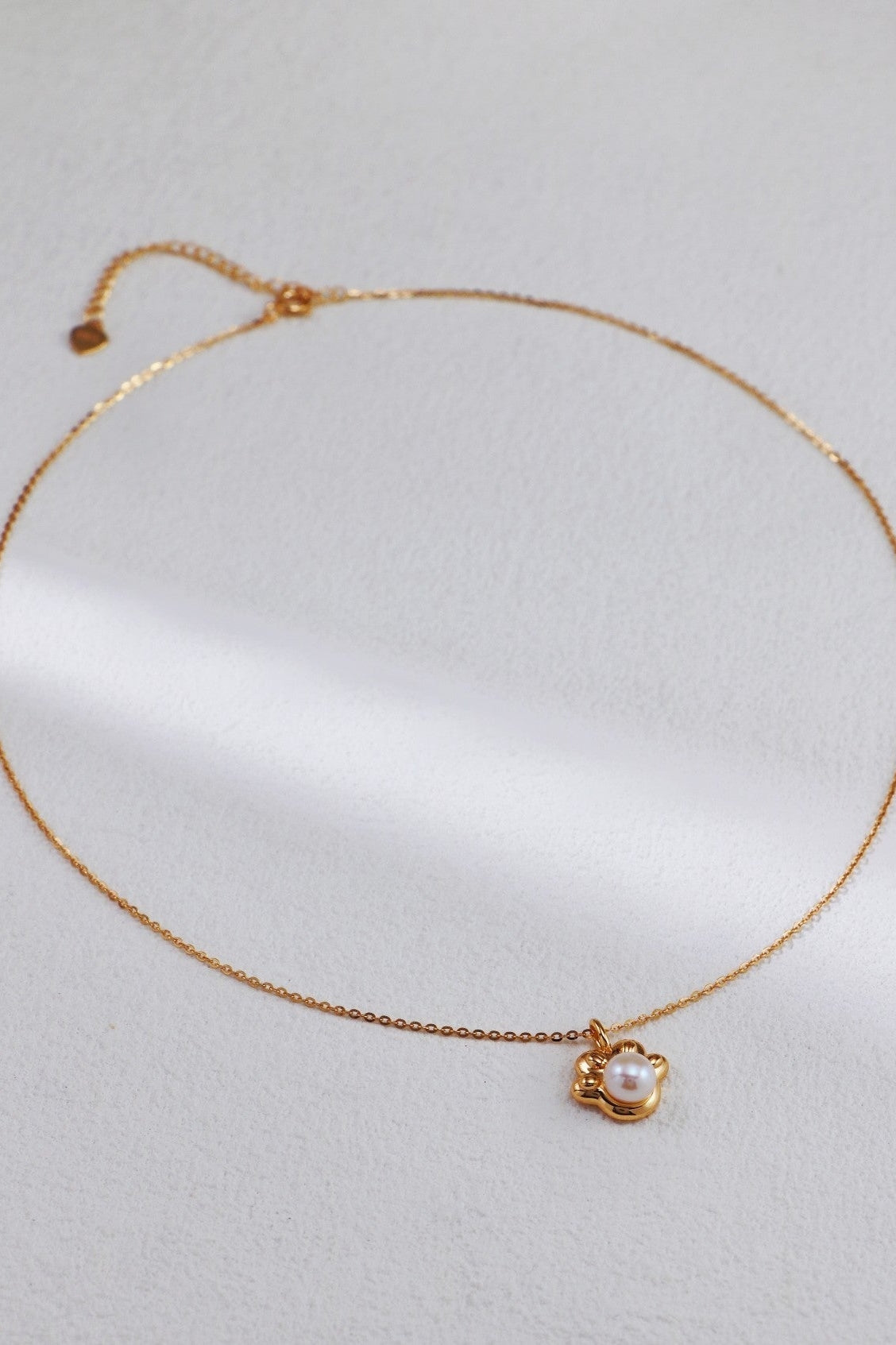 A delicate, vintage-inspired necklace from Siren Mode rests on a light-colored surface. The Elegant Pearl Pendant Necklace features an adjustable sterling silver chain and boasts a simple gold setting encasing a single, white pearl pendant.