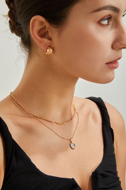 A woman in a sleeveless black top wears a gold chain necklace with a pendant and the Elegant Textured Sterling Silver Hoop Earrings by Siren Mode. She poses against a neutral background, looking to the side. Her hair is styled in an updo.