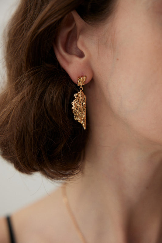 Close-up of a person with short brown hair wearing Elegant Vintage Gold Textured Leaf Drop Earrings in 925 Silver by Siren Mode. The earrings have a detailed, lacy appearance and dangle elegantly from the earlobe. The background is neutral, drawing full attention to the exquisite craftsmanship of the jewelry.