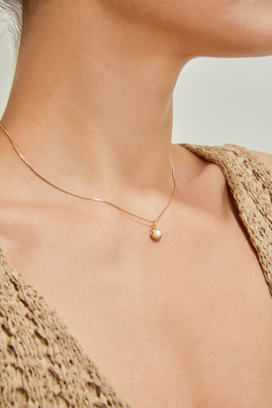 Close-up of a person wearing a Siren Mode Gold-Plated Sterling Silver Necklace with Pearl Pendant. The person is dressed in a beige, textured-knit garment with a neutral background. The image focuses on the neck and part of the collarbone area.