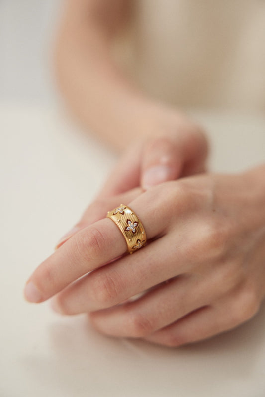 Close-up of a hand wearing the Siren Mode Luxurious Vintage Gold Adjustable Ring with Zircon Accents in 925 Silver. The ring, featuring star-shaped designs and intricate craftsmanship, is worn on the middle finger as the hand gently rests on a flat surface. The softly blurred background beautifully accentuates the exquisite details of this vintage piece.