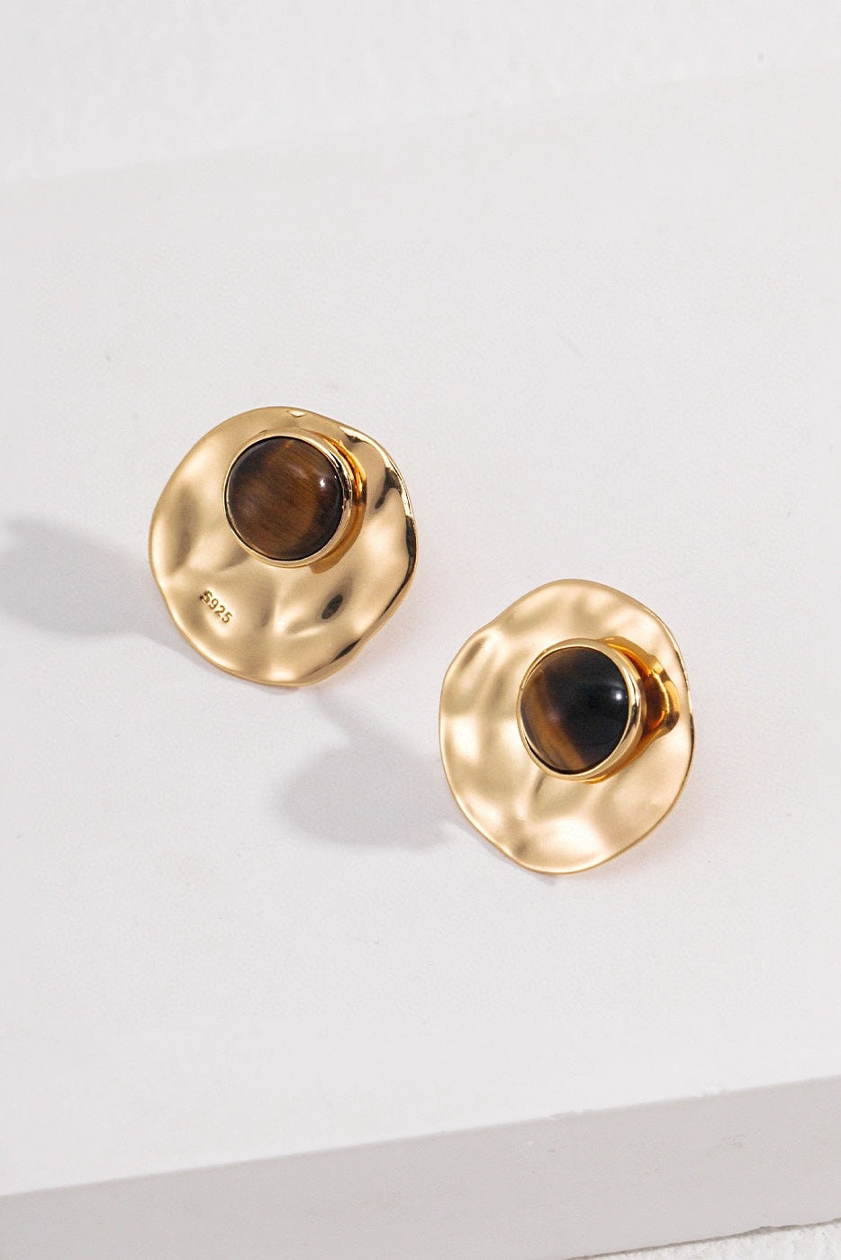 Displayed is a pair of Siren Mode's Modern Tiger's Eye Disc Earrings with a vintage gold finish. Each earring highlights a round tiger's eye gemstone set in the center. These natural gemstones rest on a white surface, casting subtle shadows.