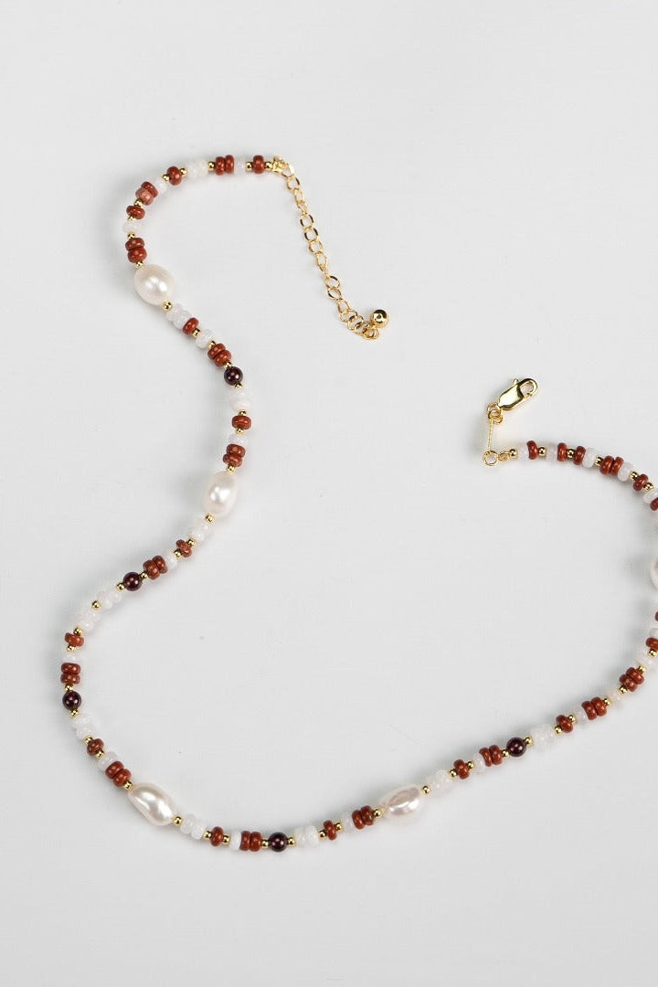 The Siren Mode Natural Pearl and Gemstone Necklace features small red and black beads interspersed with irregularly shaped white pearls in an 18K gold short beaded design. It includes a gold chain extender and a lobster clasp, all showcased against a plain white background.