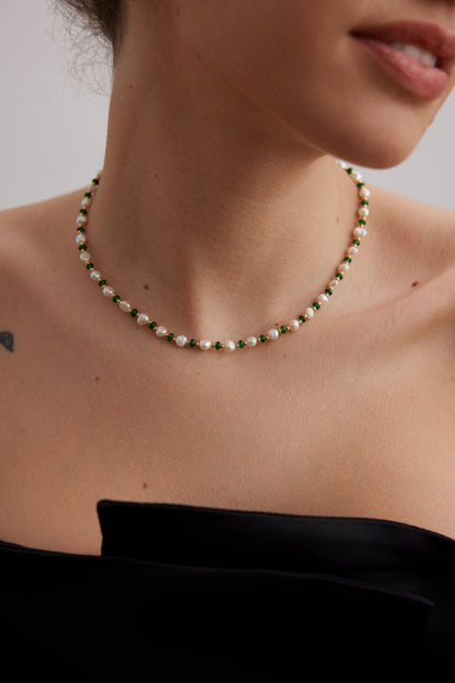 Close-up of a woman's neck adorned with the Siren Mode Natural Pearl and Green Gemstone Necklace, featuring alternating green and white beads. She is wearing a black off-the-shoulder top, with a small tattoo visible on her shoulder. Her lips are slightly parted.