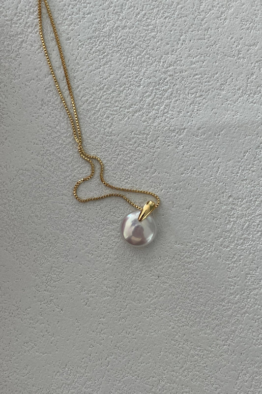 The Siren Mode Round Baroque Pearl Pendant Necklace, featuring a 14K gold-filled chain and a gold-plated sterling silver attachment, is showcased against a textured, light-colored surface.