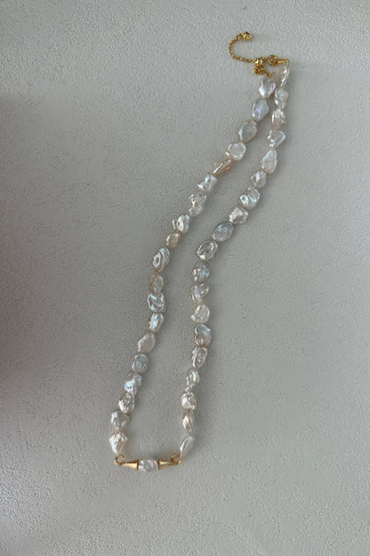 A Small Mustache Baroque Pearl Necklace by Siren Mode, featuring 18K gold plated sterling silver, lies on a white surface.