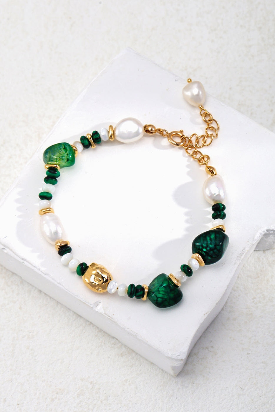 Displayed on a white background, the Siren Mode Verdant Treasure Bracelet features green and white semi-precious stones, irregular pearls, and small gold accents. This adjustable bracelet, named Vintage Gold with Natural Stones and Pearls, has a gold chain with a pearl charm at the end.