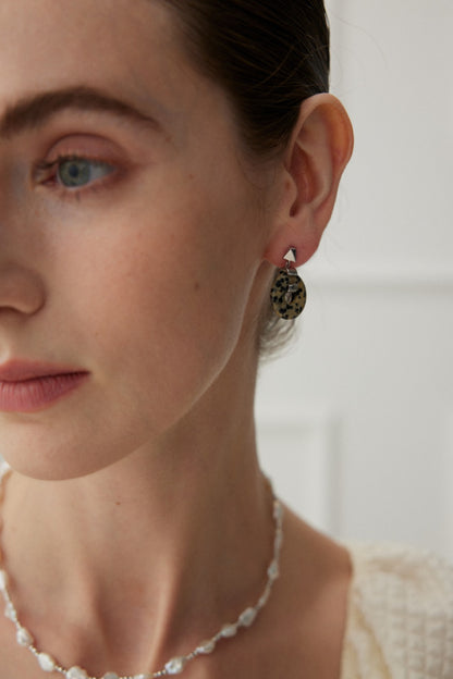 Close-up of a person's face, focusing on their left side. They wear the sleek, spotted earrings from Siren Mode's Vintage Gold 925 Silver Leopard Stone and Tiger's Eye Earrings collection, along with a delicate beaded necklace that features a shimmering Tiger's Eye pendant. The person's hair is pulled back, highlighting their smooth skin. The background is artfully blurred to draw attention to the exquisite jewelry.