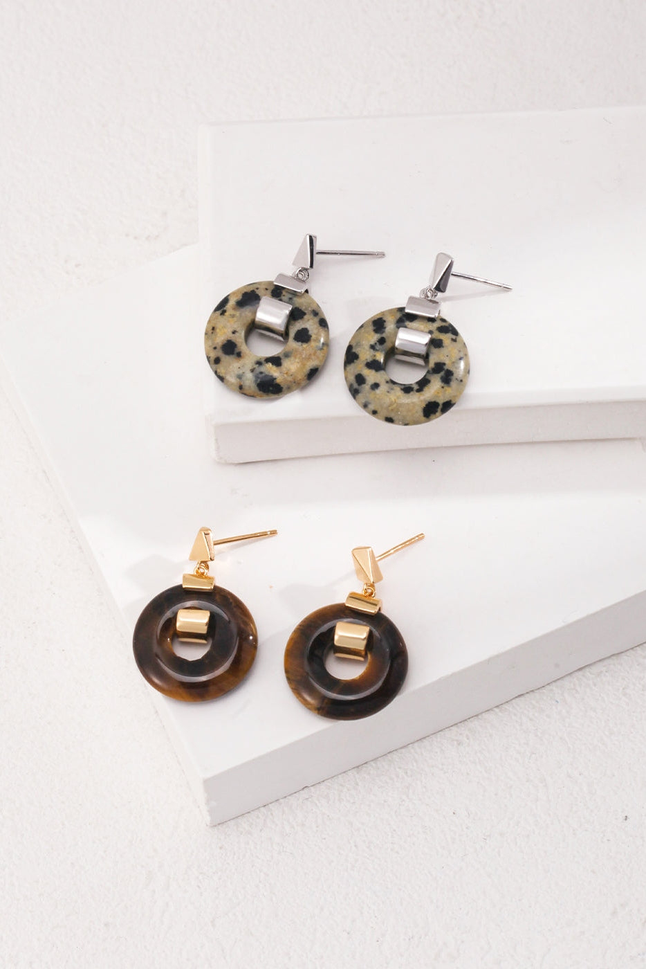 The image displays two pairs of the Vintage Gold 925 Silver Leopard Stone and Tiger's Eye Earrings by Siren Mode on white rectangular platforms. Each earring features a circular design with a rectangular bar connecting to the hook. The top pair, featuring 925 silver hooks, has a beige and black spotted Leopard Stone pattern, while the bottom pair highlights a brown and black marbled Tiger's Eye pattern.