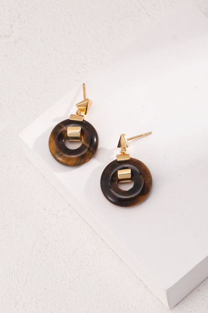 The Vintage Gold 925 Silver Leopard Stone and Tiger's Eye Earrings by Siren Mode, featuring round, brown tortoiseshell rings and gold triangular studs accented with 925 silver, are displayed on a minimalist white surface. The earrings' modern design contrasts with the simple, textured background.