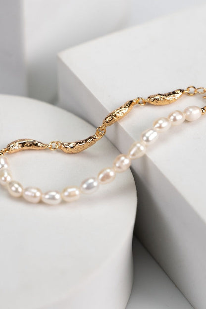 The Siren Mode Vintage Gold 925 Silver Natural Pearl Bracelet, featuring a delicate arrangement of small natural pearls on a textured 925 silver chain, is elegantly displayed on a minimalist white stone backdrop. Geometric shapes subtly visible in the background enhance its luxurious and elegant design.