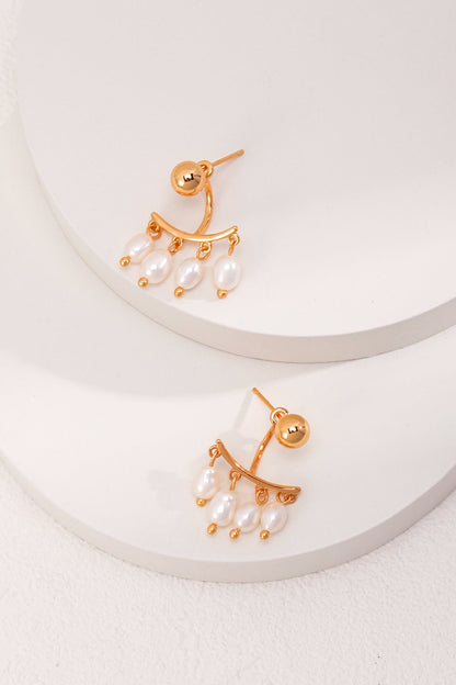 A pair of Siren Mode Vintage Gold 925 Silver Natural Pearl Drop Earrings lie on two white circular platforms. Each earring features a round gold stud with a curved gold bar hanging below, adorned with five small natural pearls suspended at the bottom. The minimalist background enhances the sophisticated design.