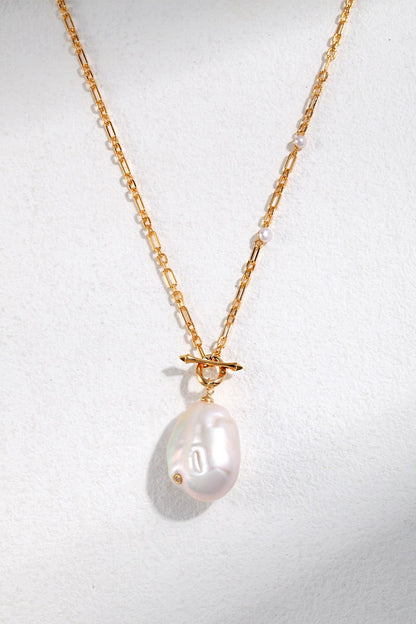 A close-up of the Siren Mode Vintage Gold 925 Silver Natural Pearl and Zircon Pendant Necklace featuring a large, irregularly shaped natural pearl pendant. The chain, composed of small links with occasional tiny beads, is accented by a gold loop securing the pendant. The background is a soft, light grey color.