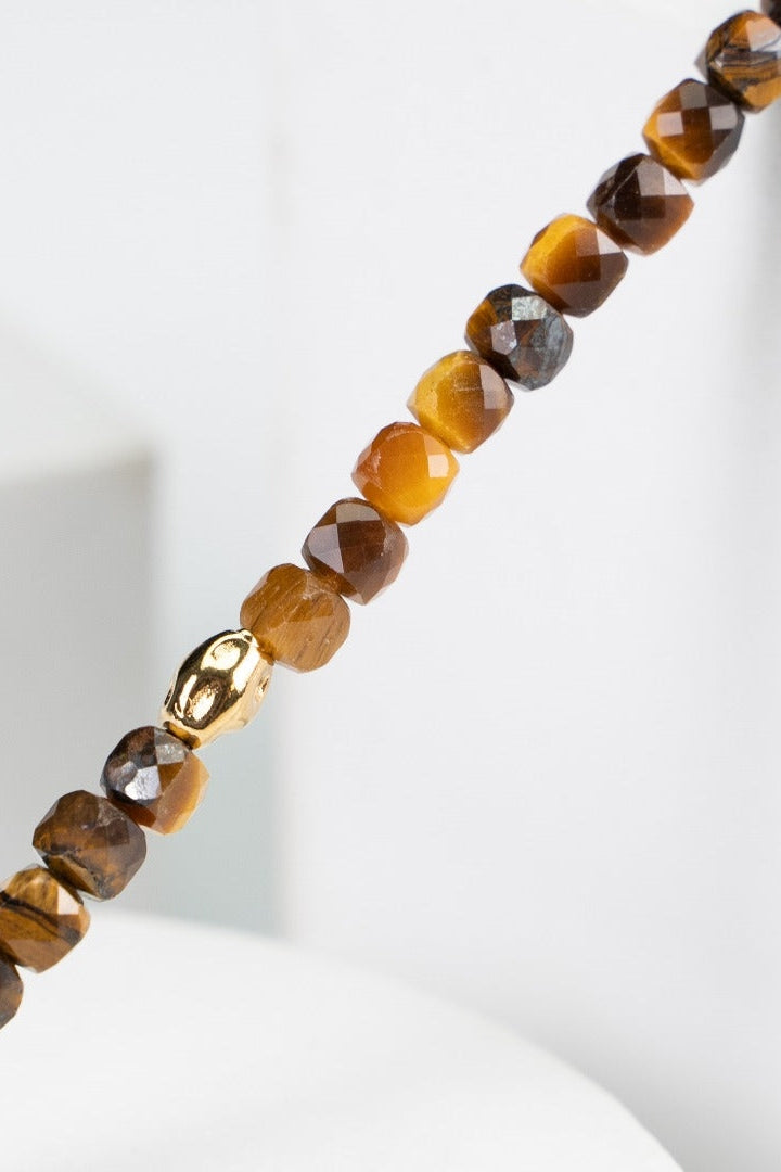 Close-up of Siren Mode's Vintage Gold 925 Silver Tiger's Eye Beaded Bracelet, showcasing small, faceted beads in shades of brown, yellow, and gray strung together in a uniform pattern. A single 925 silver tiger's eye bead stands out prominently among them. The background is white and minimalist.