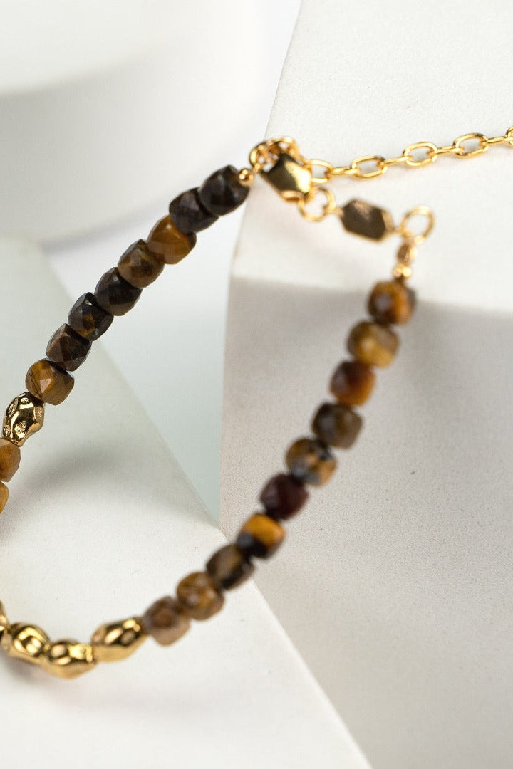 A close-up of the Siren Mode Vintage Gold 925 Silver Tiger's Eye Beaded Bracelet, showcasing its alternating brown and gold beads with accents of 925 silver. The bracelet includes a gold chain extender with a small charm at the end, all elegantly placed on a white surface with minimalistic geometric shapes in the background.