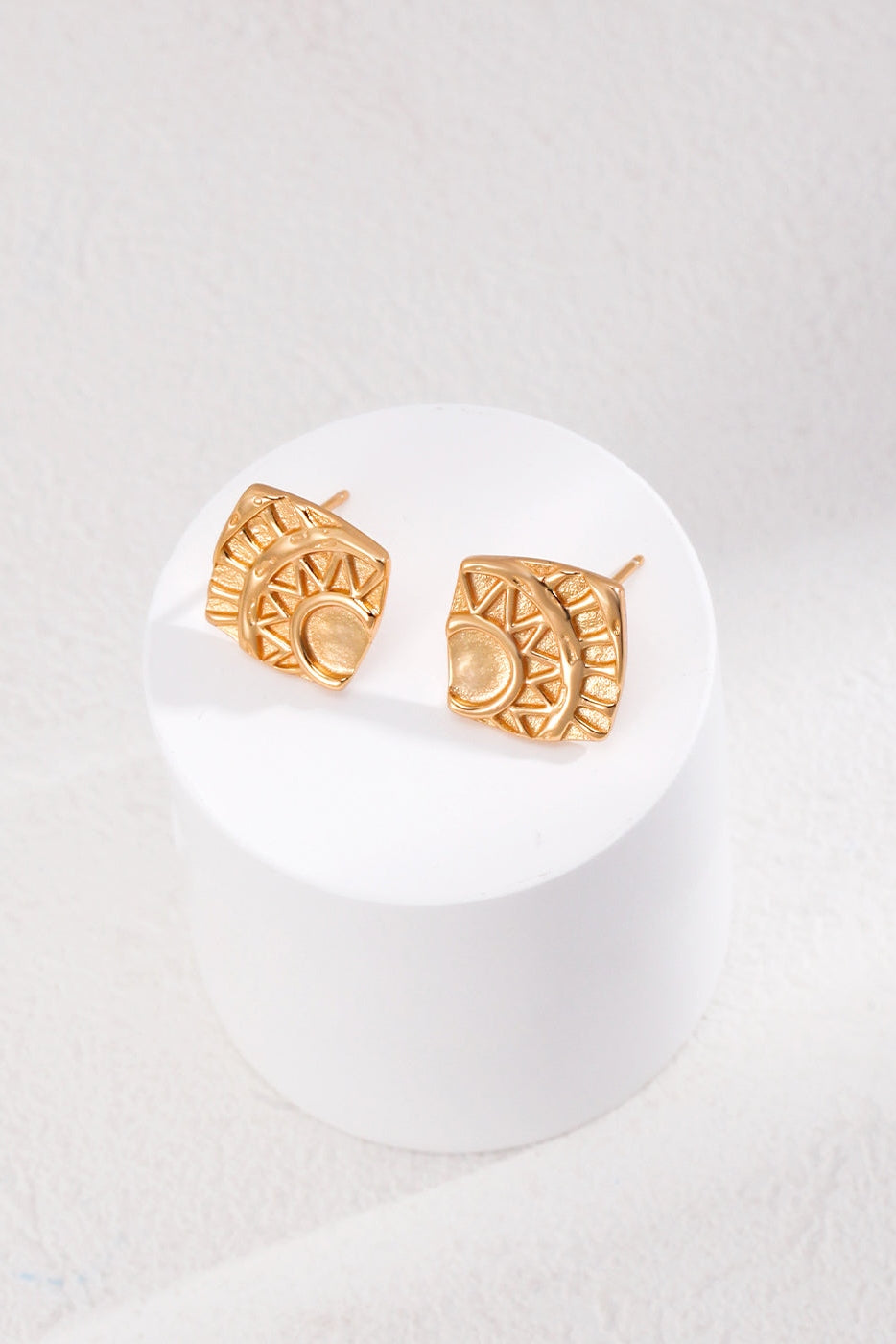 The Vintage Gold Geometric Stud Earrings by Siren Mode feature semi-circular shapes and triangular designs, crafted from 925 silver. They are elegantly displayed on a white circular platform against a light textured background.