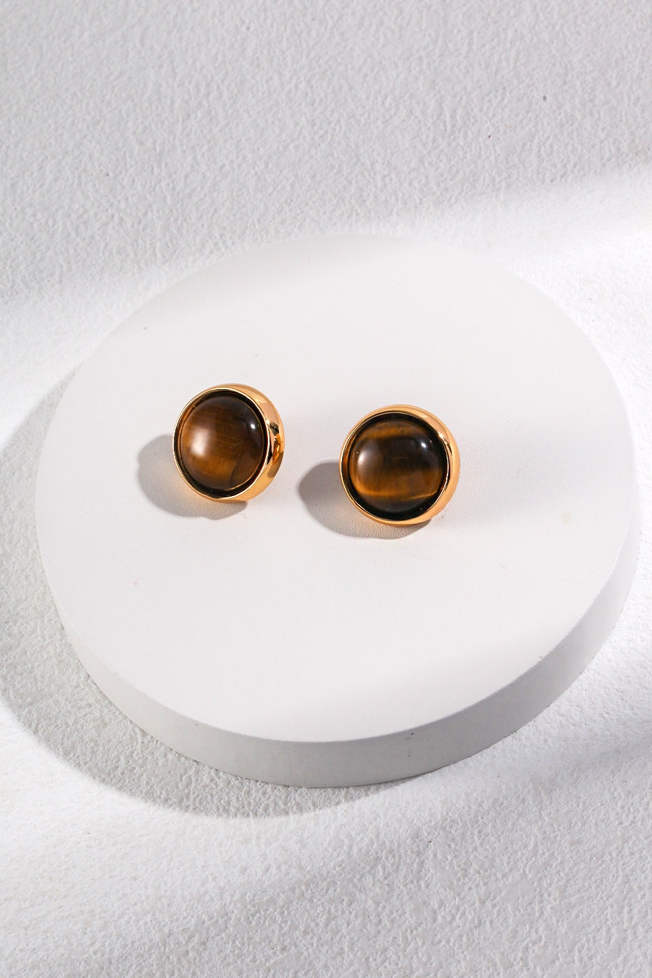 Siren Mode presents the Vintage Gold Tiger's Eye Stud Earrings, showcased on a white circular platform against a light gray background. These round, gold-rimmed stud earrings feature dark brown, glossy Tiger's eye gemstones, with an elegant and simple design that highlights the polished stones encased in gold.