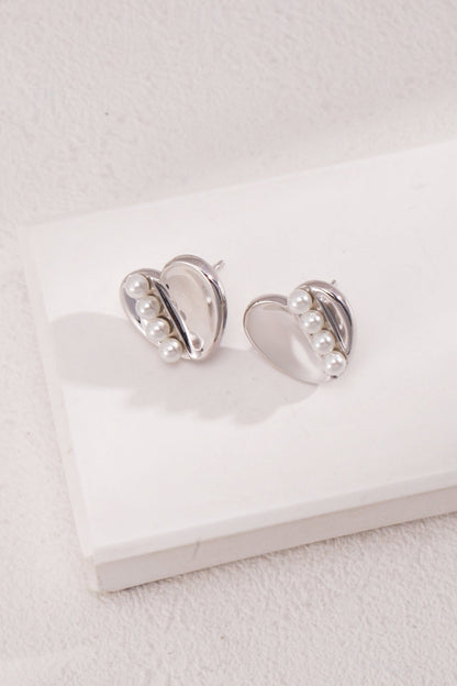 Siren Mode presents the Vintage Gold and White Gold 925 Silver Heart Pearl Stud Earrings, featuring three small white pearls arranged in a row on each heart-shaped piece. These elegant earrings are showcased gracefully on a white, slightly textured surface.