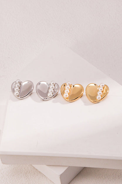 A pair of Siren Mode Vintage Gold and White Gold 925 Silver Heart Pearl Stud Earrings, each heart-shaped and adorned with three small pearls on one side, are placed on a white surface with a slightly textured backdrop.