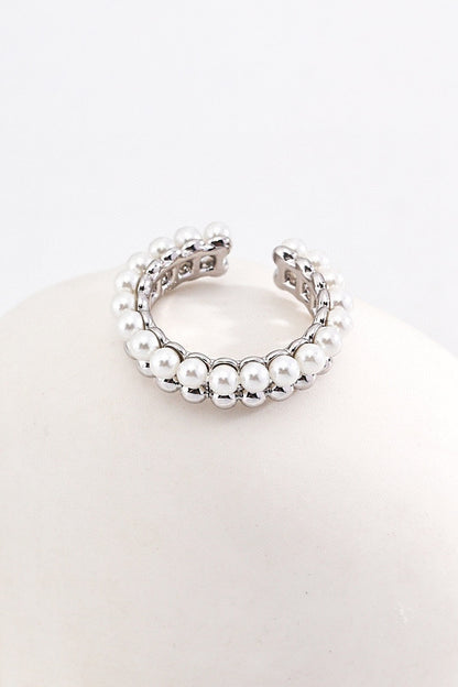 A silver open cuff bracelet adorned with two rows of white pearls is displayed on a smooth, white surface. The elegant design and lustrous pearls of this bracelet exude a sophisticated and timeless appeal, mirroring the charm found in Siren Mode's Vintage Gold and White Gold 925 Silver Pearl Beaded Rings.