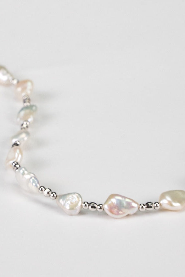 A close-up of a delicate Siren Mode White Gold 925 Silver Baroque Pearl Necklace showcases irregularly shaped baroque pearls interspersed with small silver beads, all elegantly arranged on a white background.