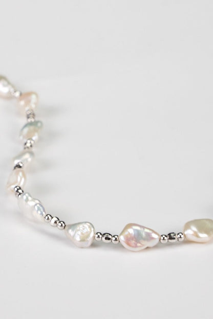 A close-up of a delicate Siren Mode White Gold 925 Silver Baroque Pearl Necklace showcases irregularly shaped baroque pearls interspersed with small silver beads, all elegantly arranged on a white background.