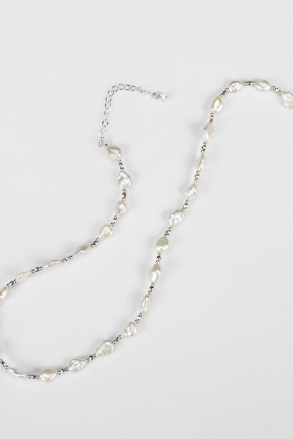 The Siren Mode White Gold 925 Silver Baroque Pearl Necklace showcases an array of uniquely shaped baroque pearls, interspersed with delicate metallic beads. It is secured with a silver-tone lobster clasp and features an adjustable chain extender, all elegantly displayed against a plain white background.